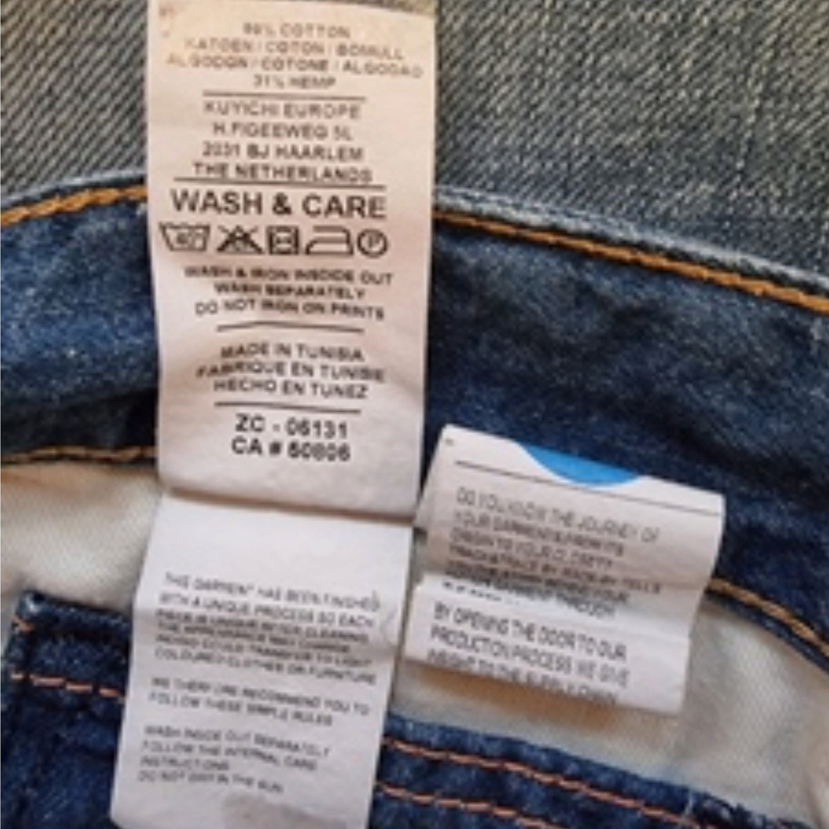 Close-up of a blue denim garment showing the inner waistband and two sewn-on care labels, including one that reads KUYCIH.