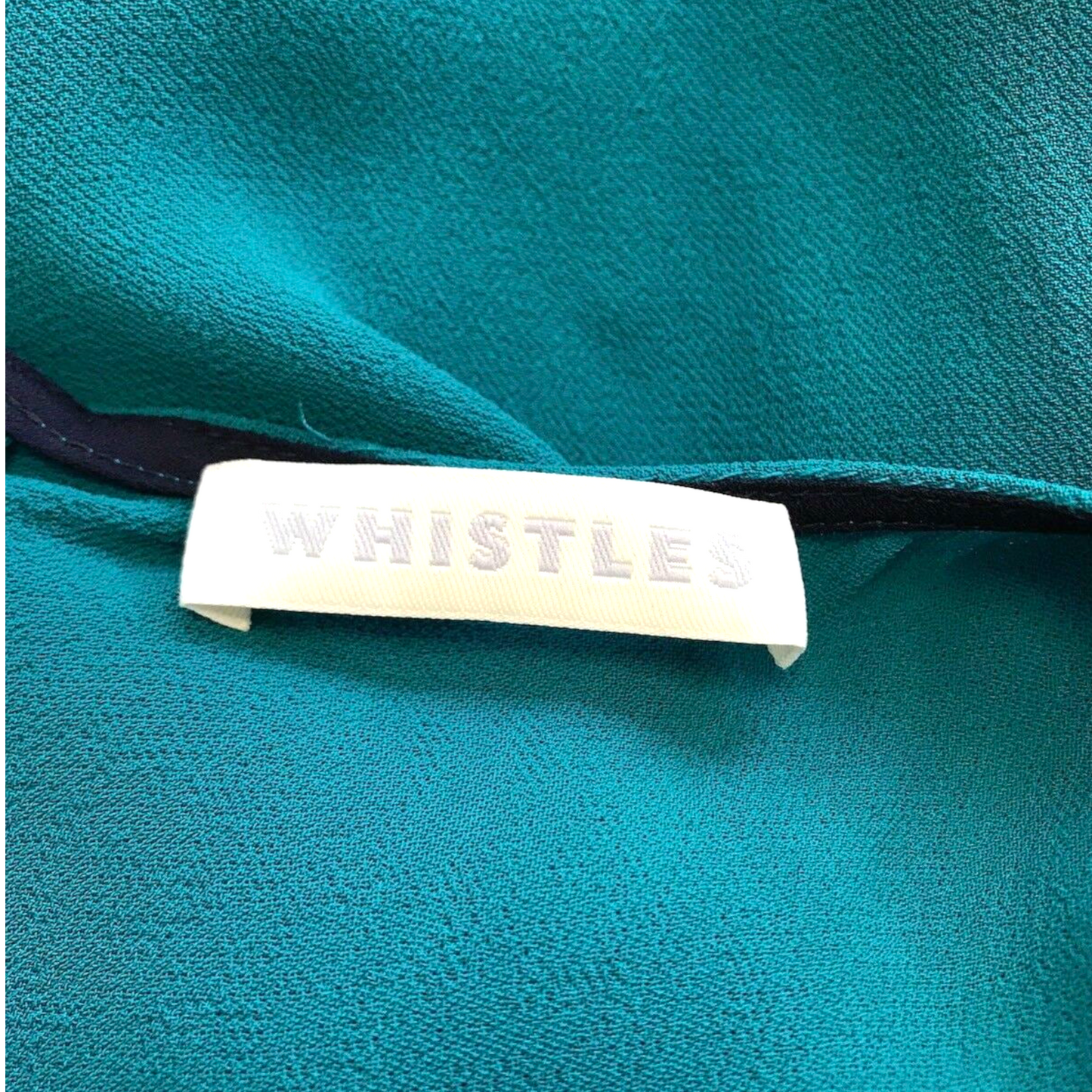 Teal fabric with a 'Whistles' label on a close-up of clothing.