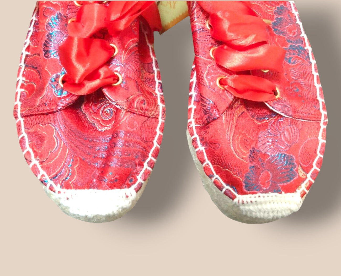 Red embroidered shoes with white soles on a beige background
