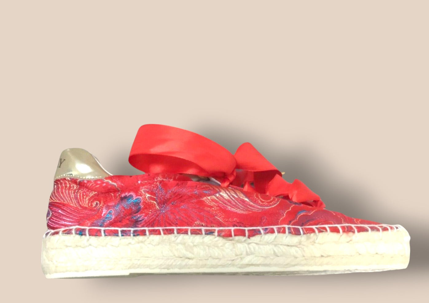 Red sneaker with floral pattern and bow on a beige background