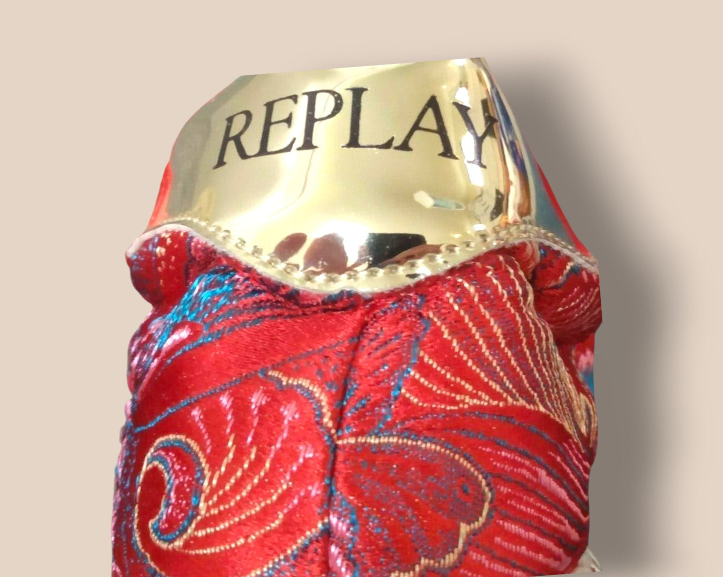 Red patterned product with gold 'REPLAY' label on a beige background