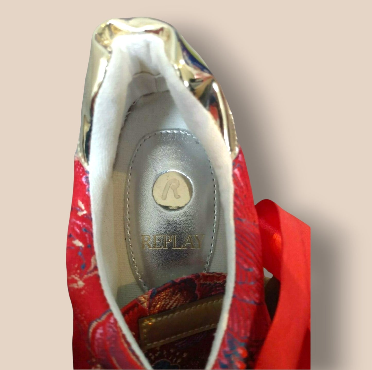 Close-up of a red shoe with 'Replay' branding on a beige background