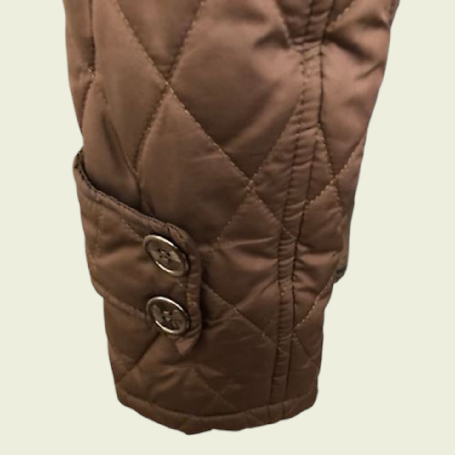 Close-up of a brown quilted jacket sleeve with buttons on a beige background
