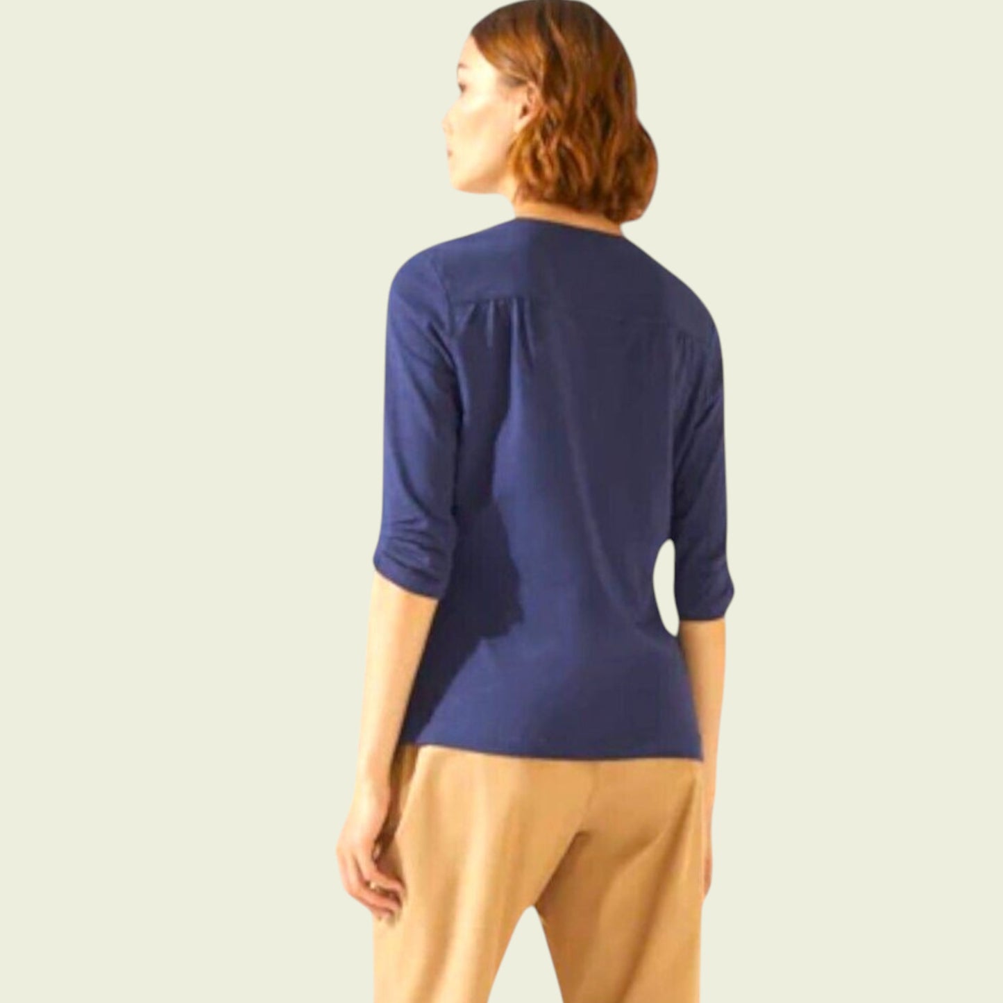 Woman wearing a blue top and beige pants on a light background