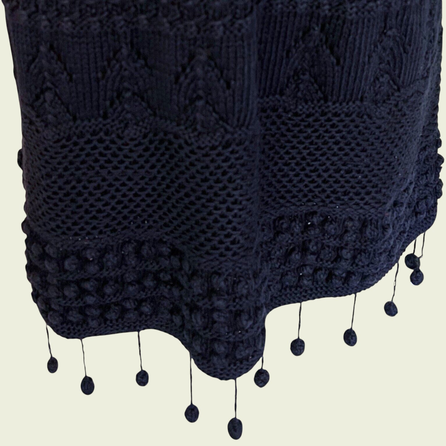 Close-up of a dark blue knitted garment with tassels on a beige background