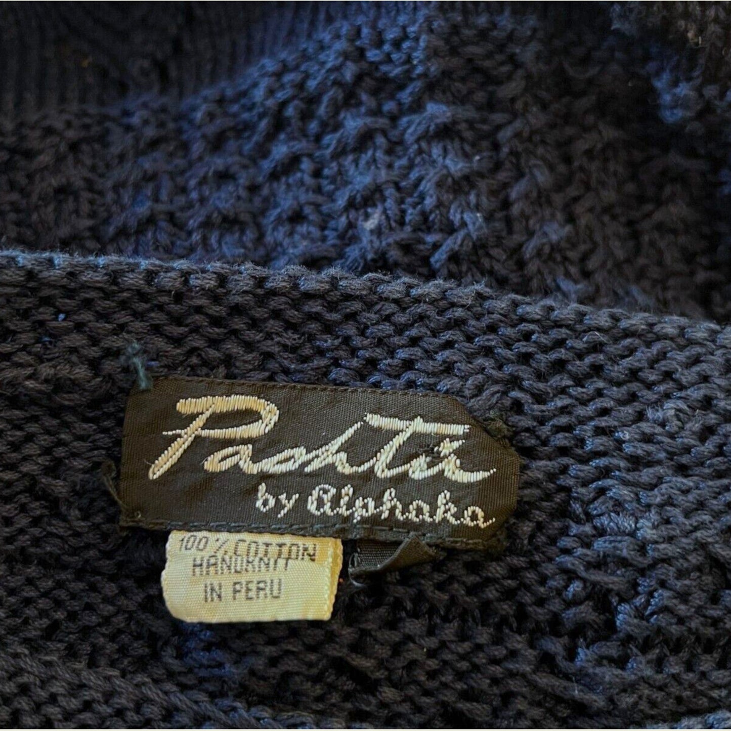 Close-up of a label on a dark blue knitted fabric, featuring 'Pashtie' by Alphaka' branding.