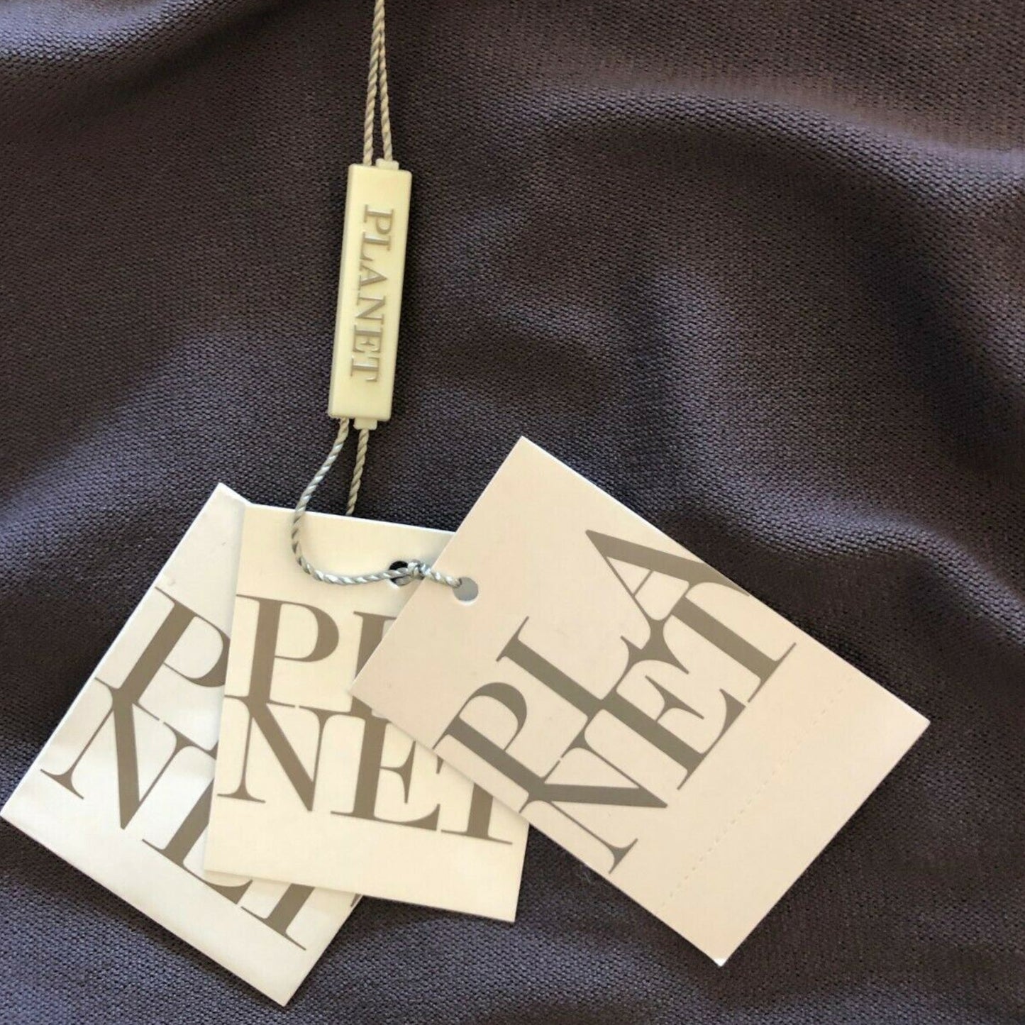 Two beige 'PLANET' tags hanging against a dark fabric background
