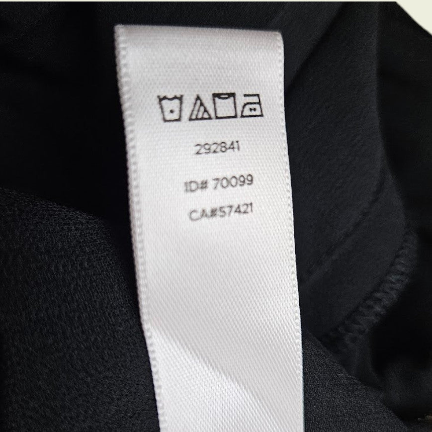 Close-up of a clothing label with care instructions and numbers on a dark fabric background.