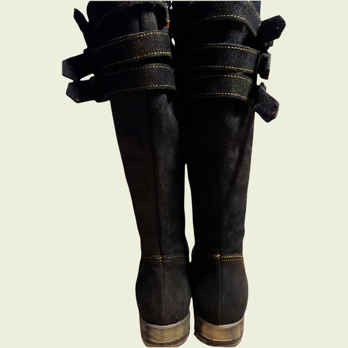 Dark leather boots with decorative straps on a beige background