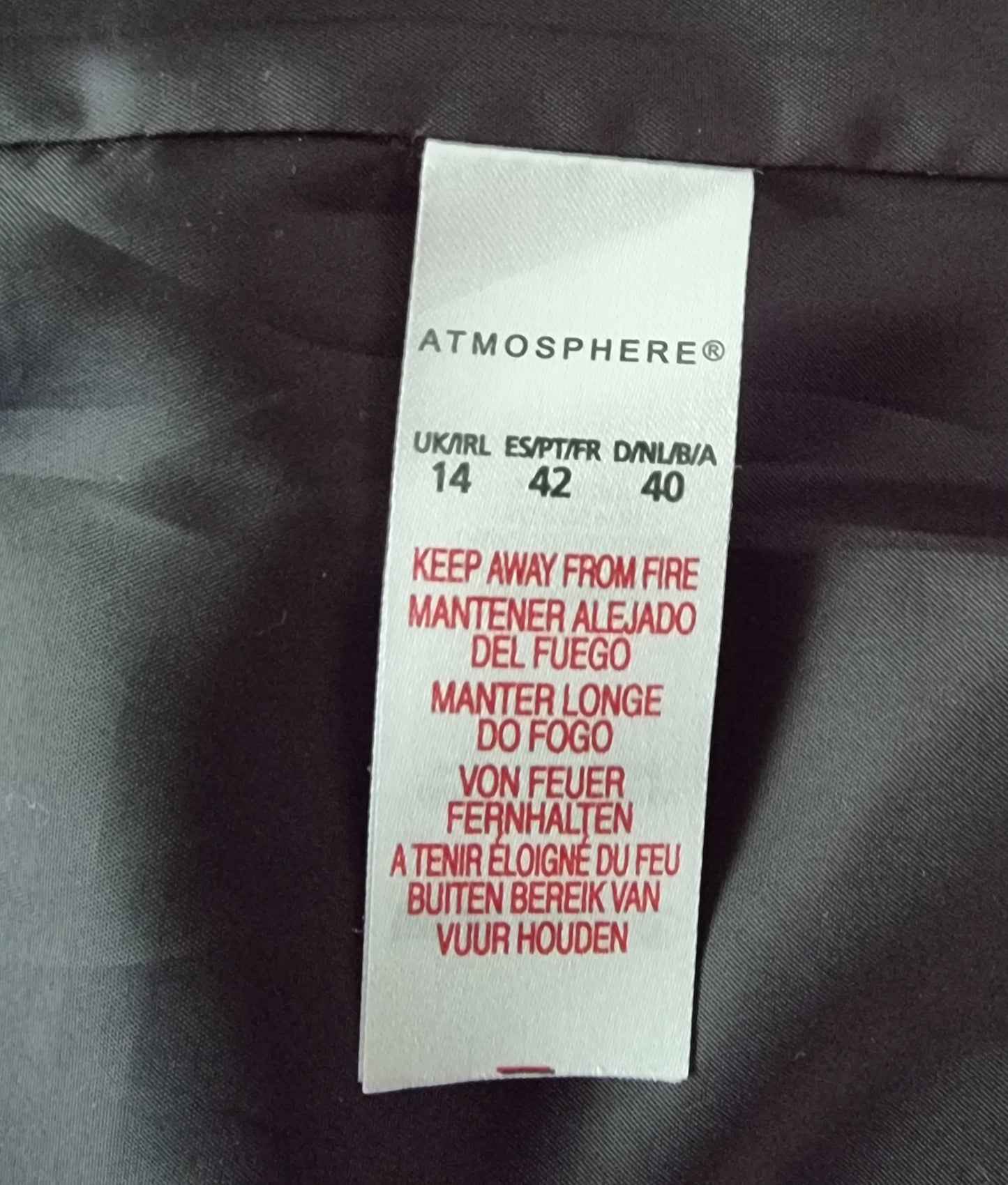 Clothing label on a dark fabric background with 'Atmosphere' branding.