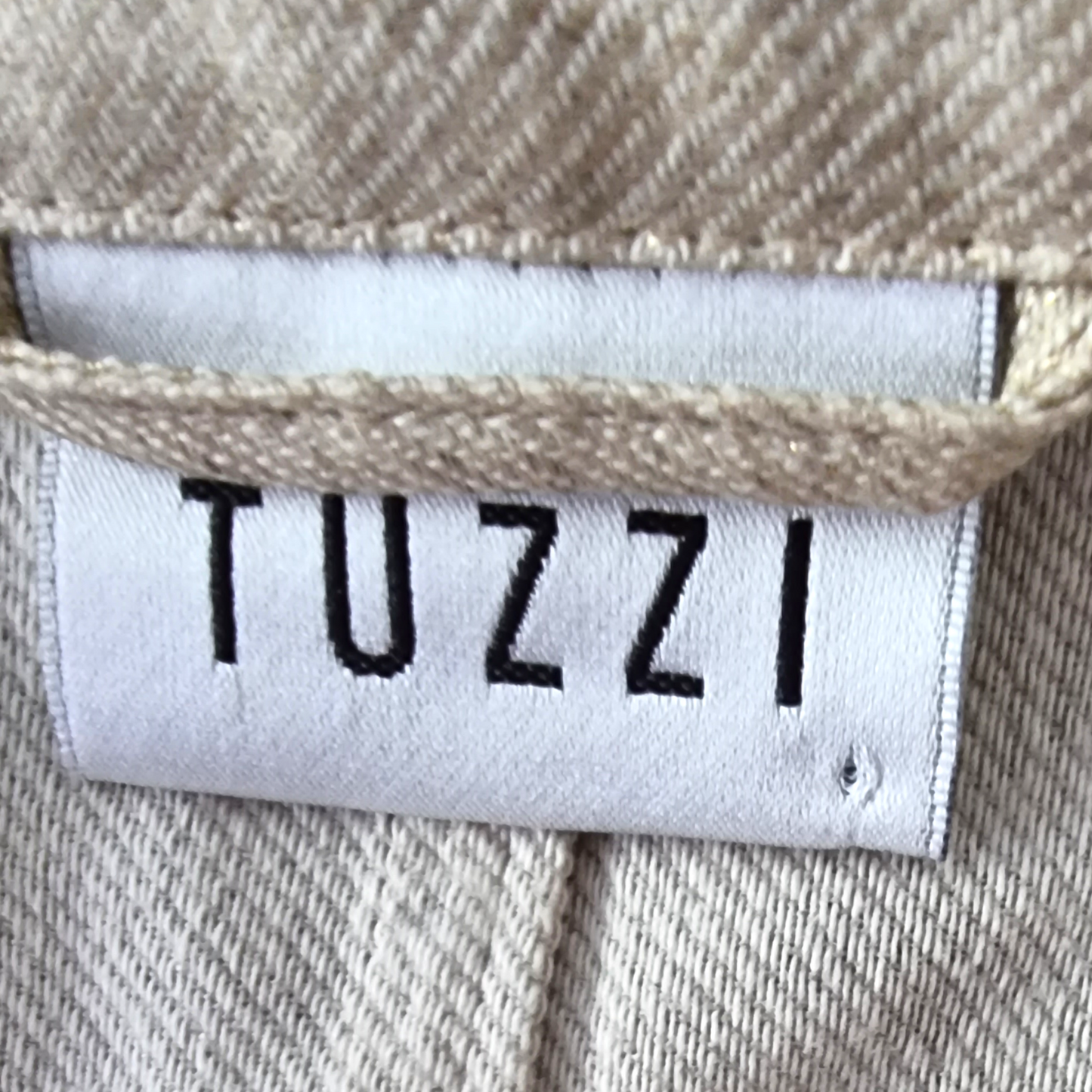 Close-up of a 'TUZZI' label on beige fabric.