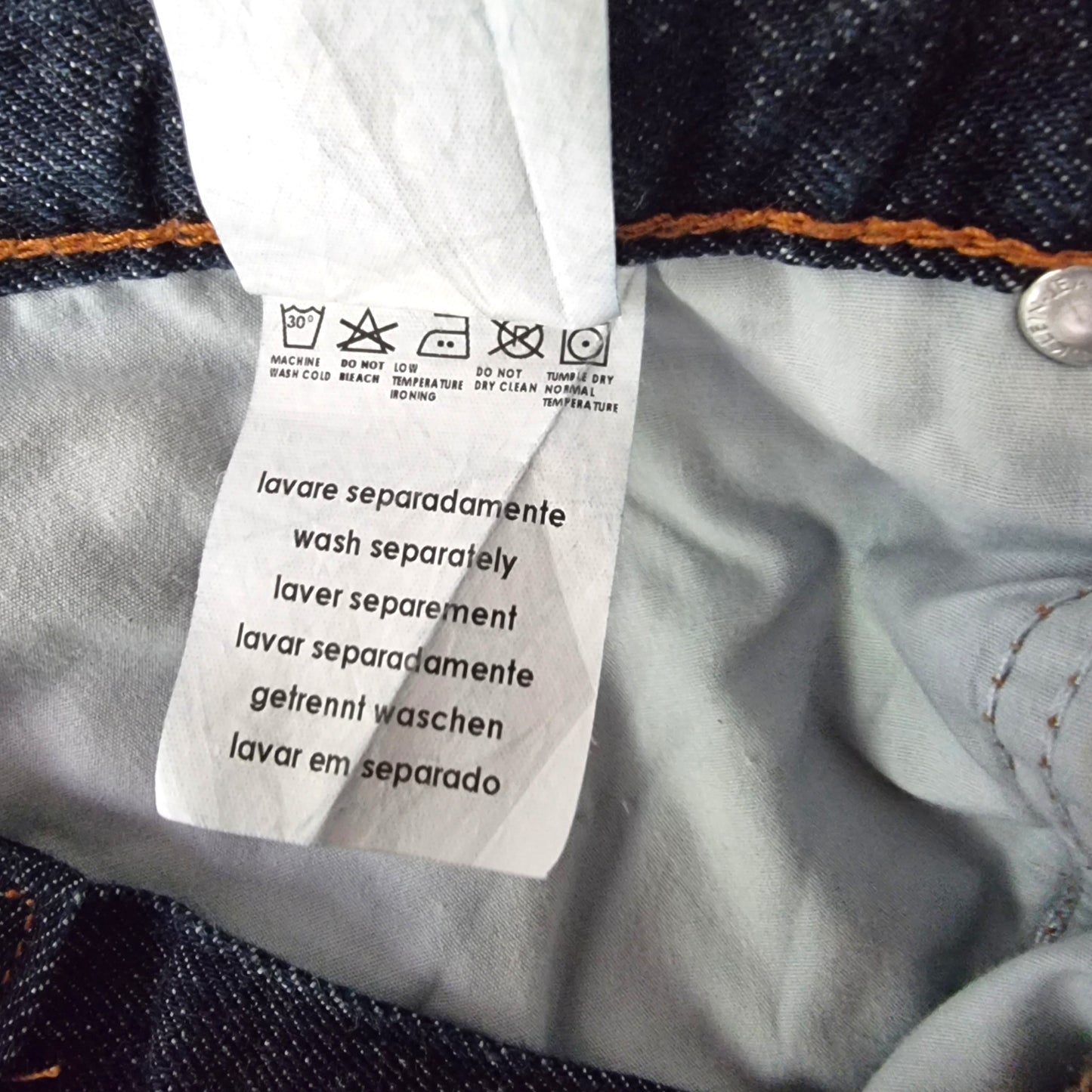 Close-up of a clothing label on denim fabric with washing instructions.