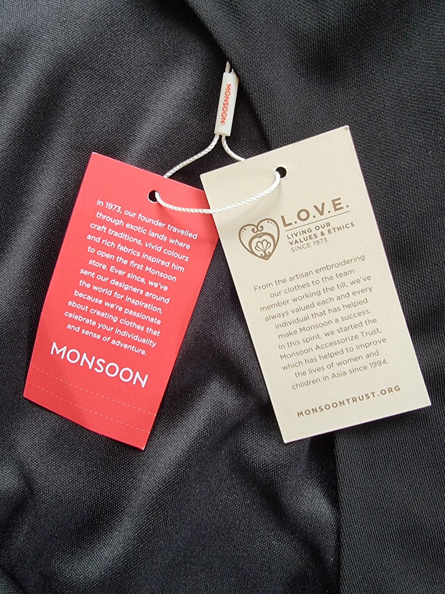 Two clothing tags, one red and one beige, on a dark fabric background.