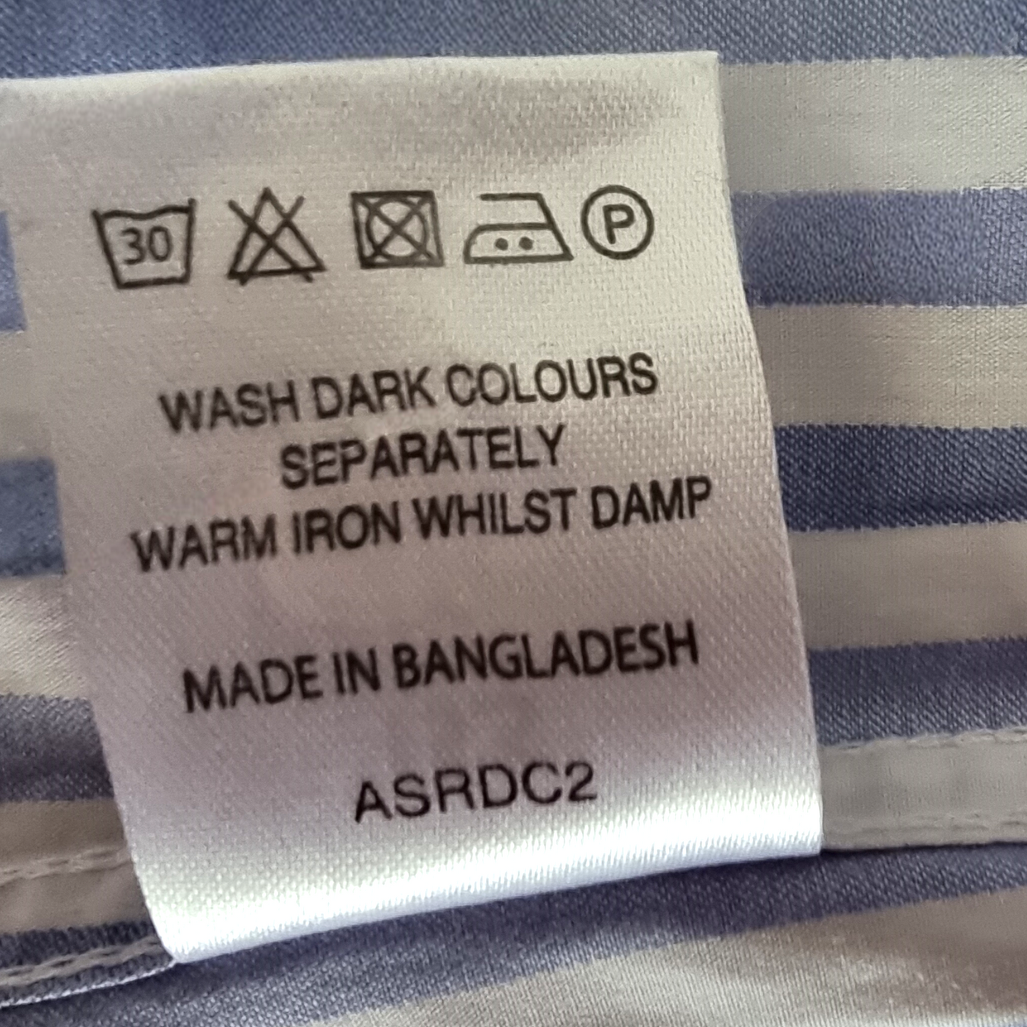 Clothing label with washing instructions and product details on a striped fabric background