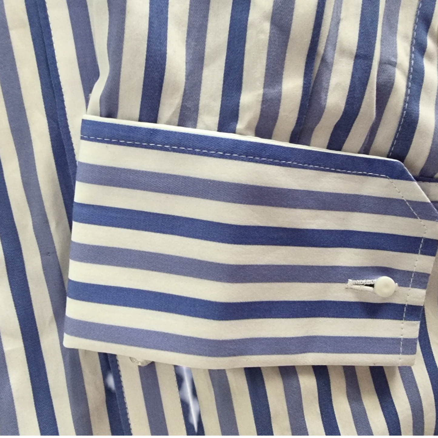 Close-up of a blue and white striped shirt with a cuff and button.
