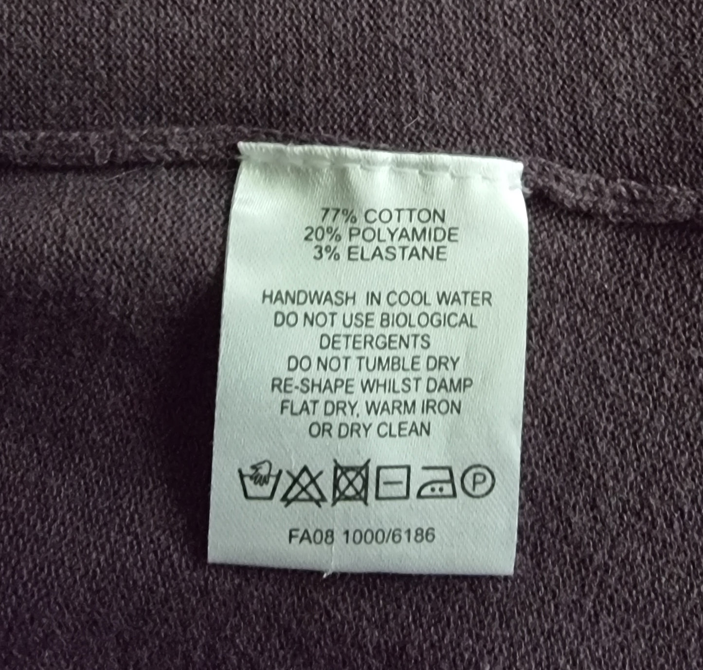 Clothing label with fabric composition and care instructions on a dark fabric background