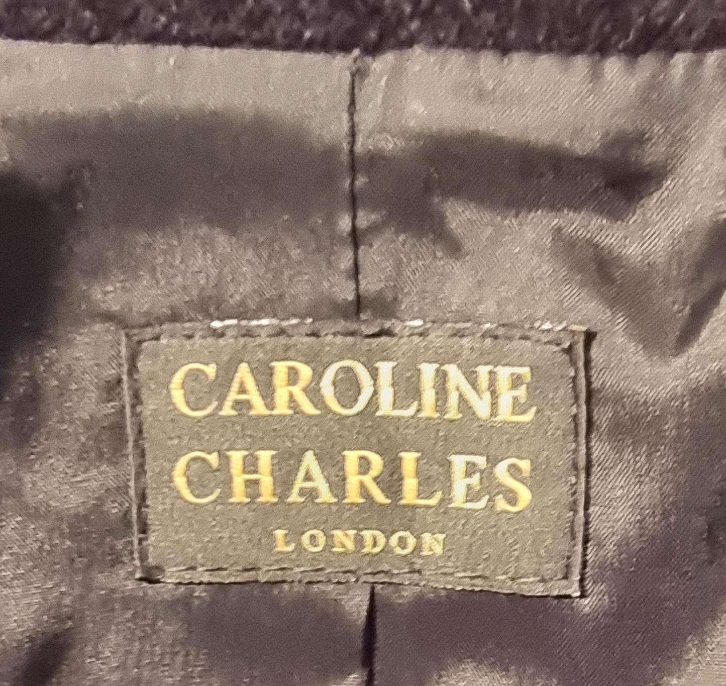 Label with 'Caroline Charles London' on a textured fabric background