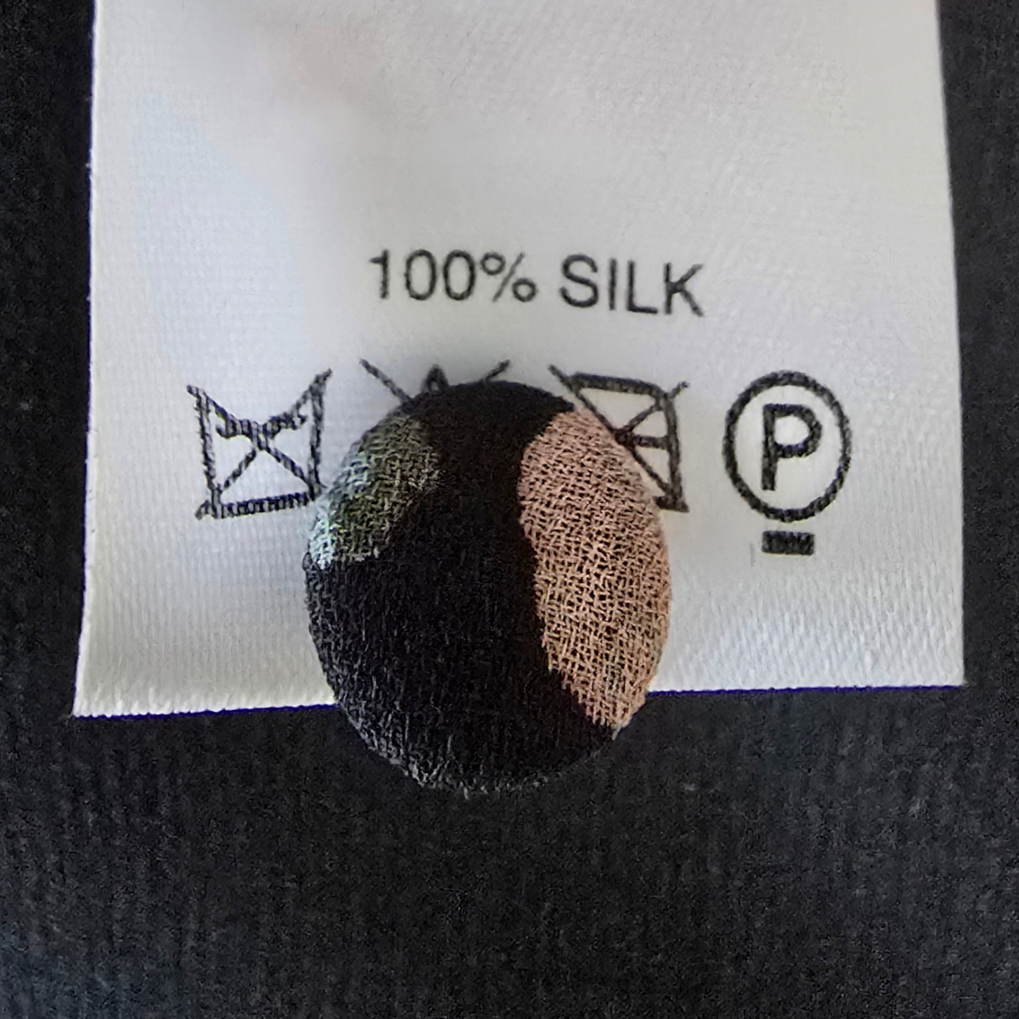 Garment label showing 100% silk and spare button on black background