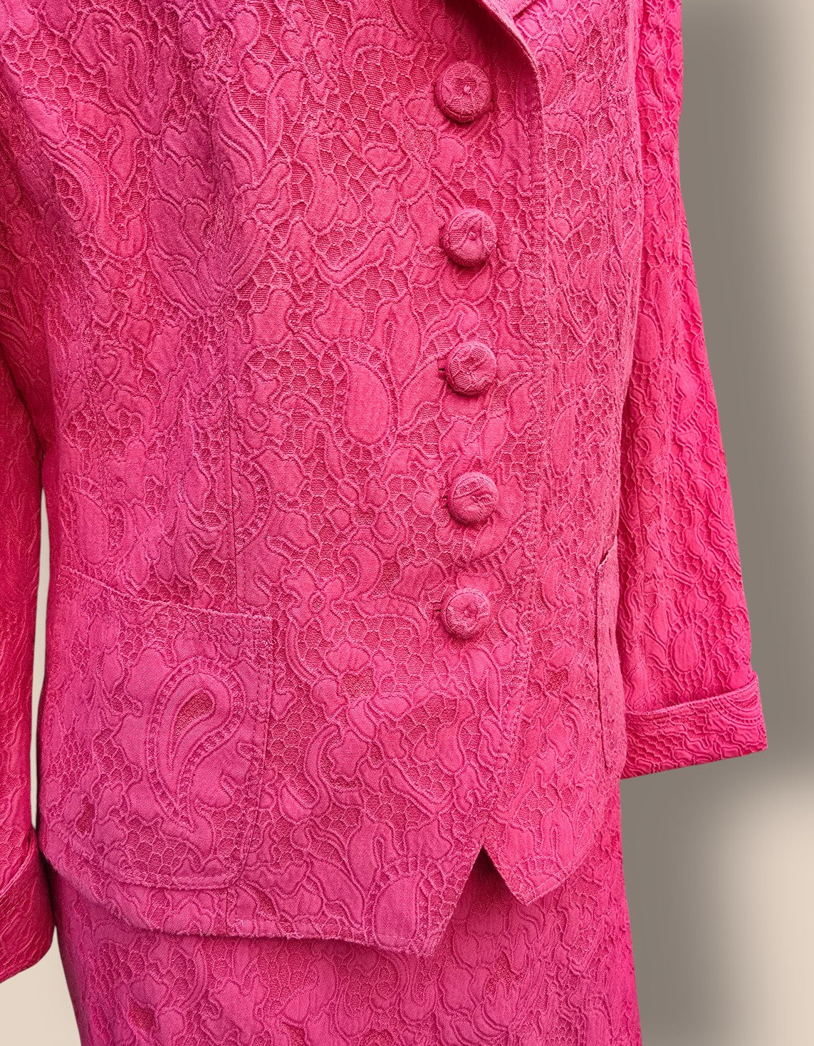 Close-up of a pink textured garment with buttons on a neutral background