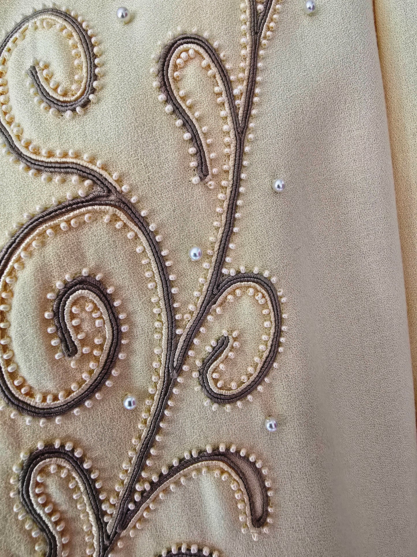 Close-up of intricate beadwork on a yellow fabric surface