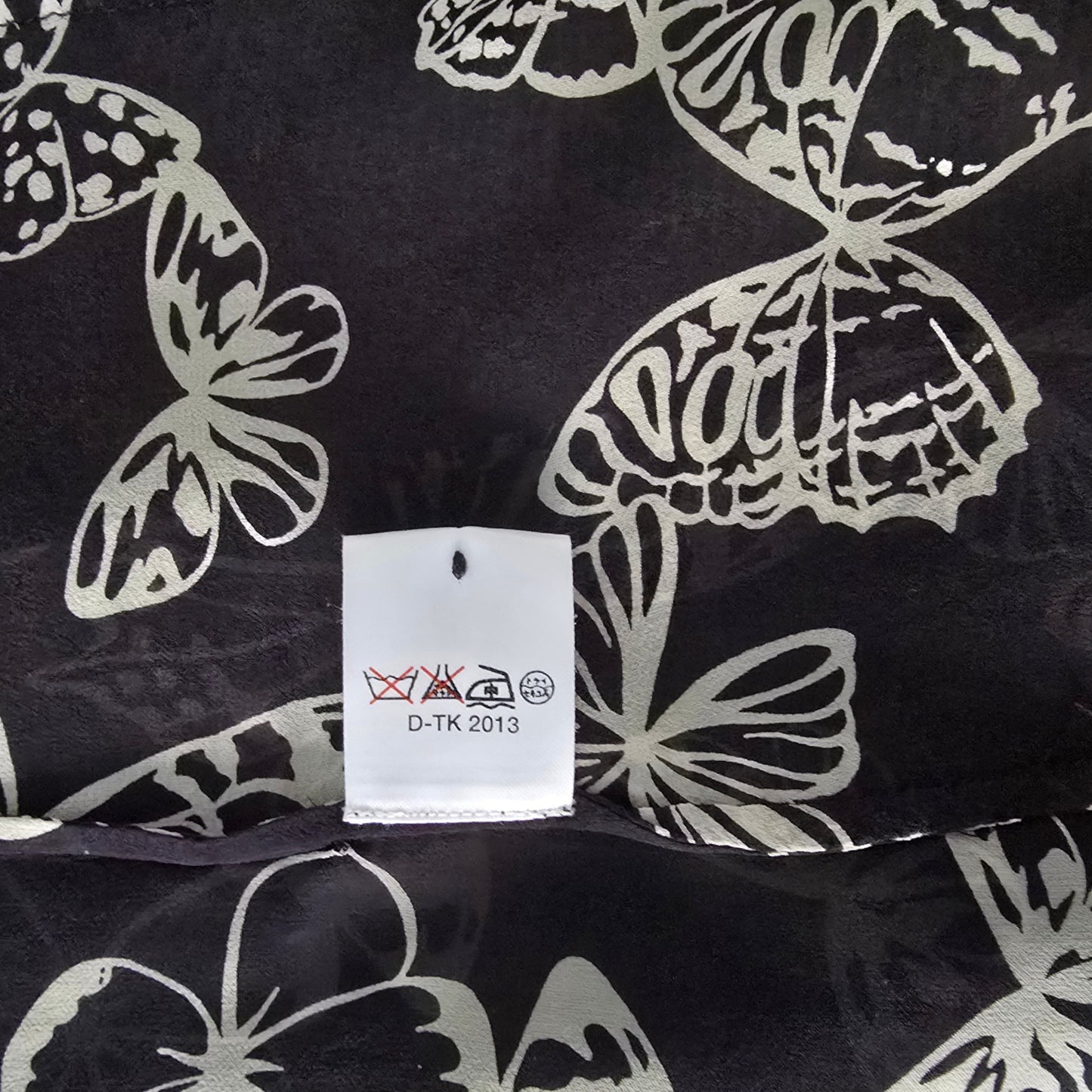 Black fabric with white butterfly patterns and a tag displaying text and symbols.