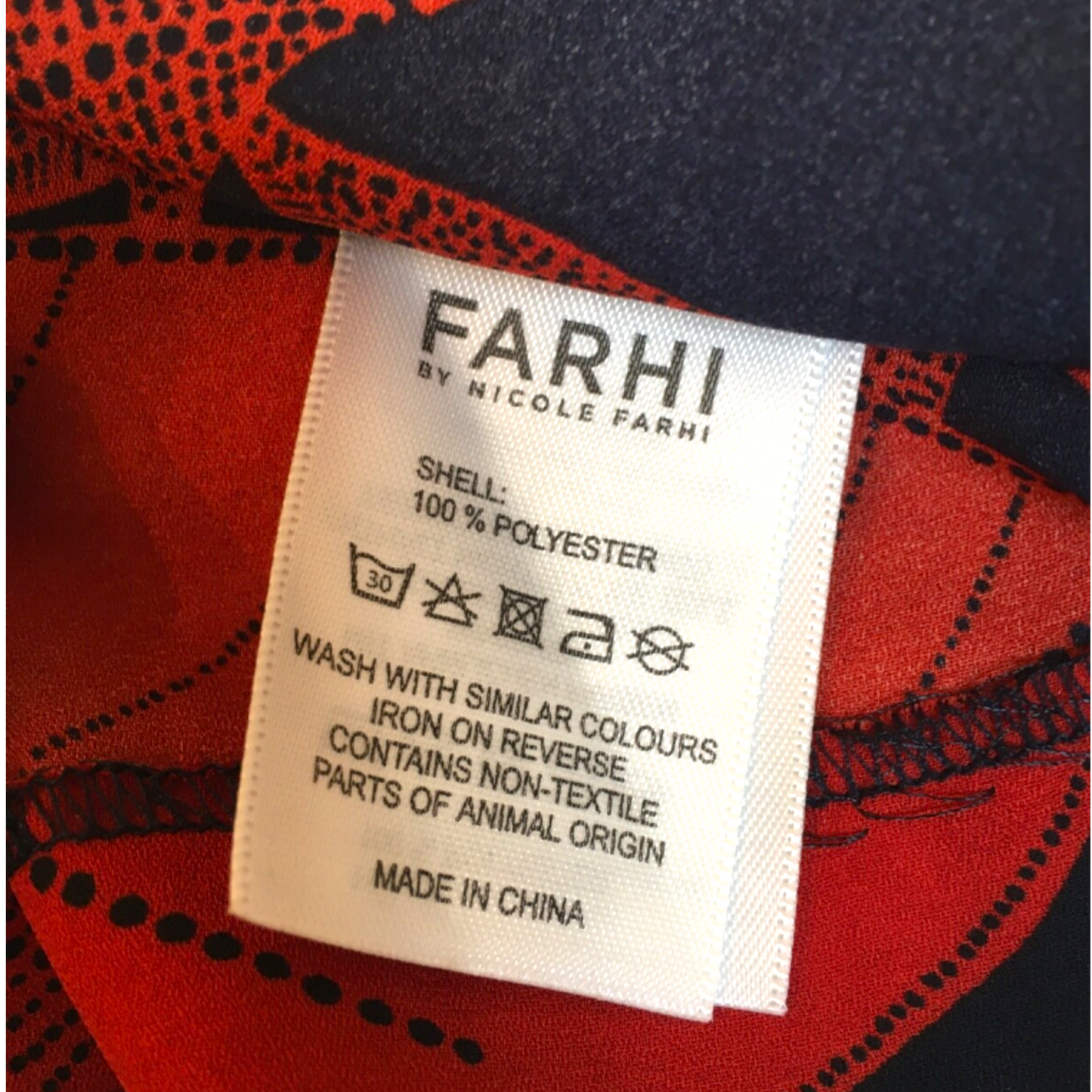 Fabric label with 'FARHI' branding on a red and black patterned fabric background