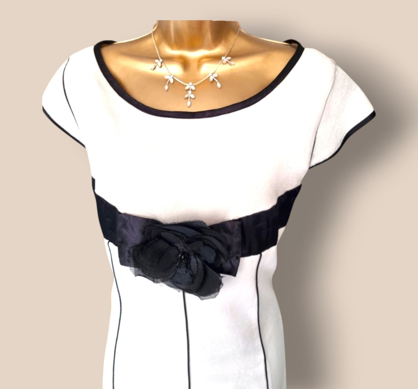 White dress with black trim and bow on a mannequin against a beige background