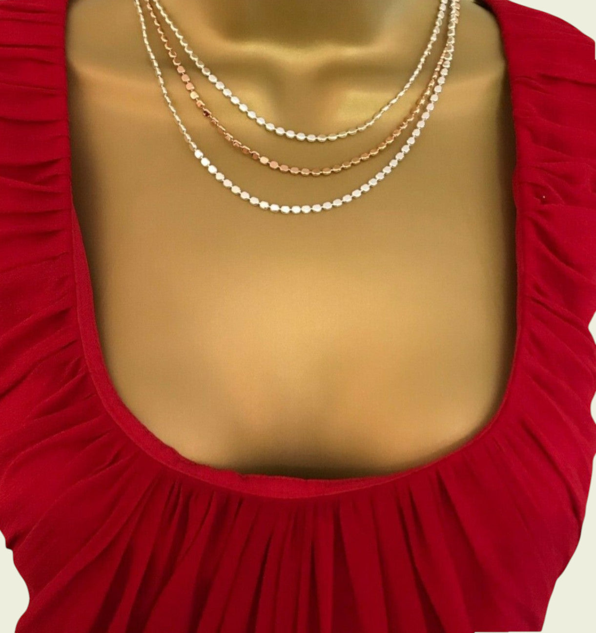 Mannequin wearing a red dress with gold necklaces on a plain background