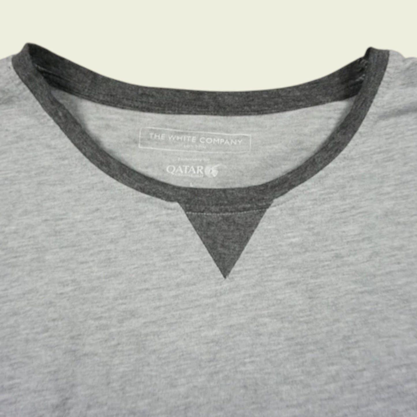 Gray shirt with black trim and visible brand logo on a beige background
