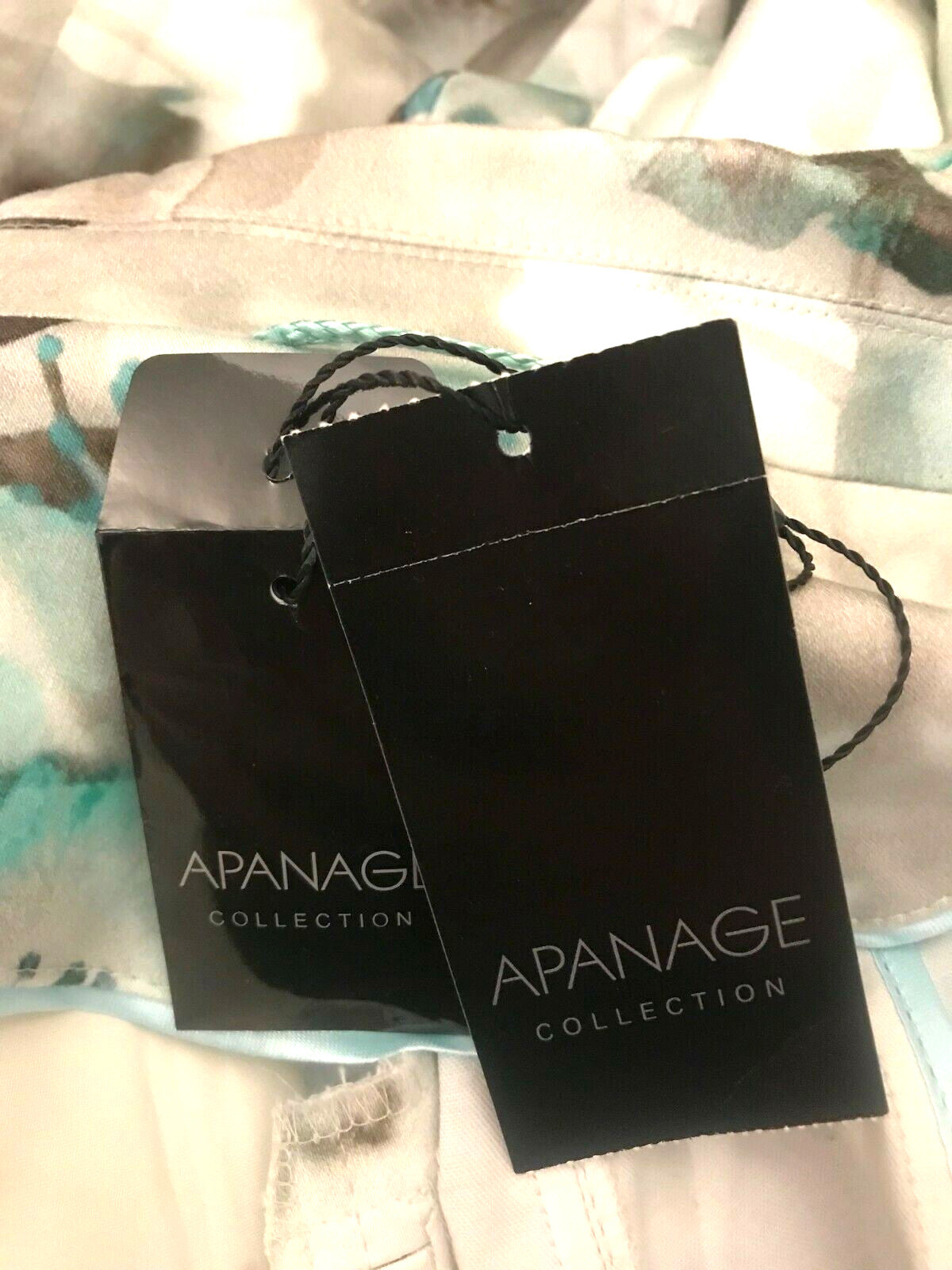 Two black APANAGE Collection tags on a patterned fabric background