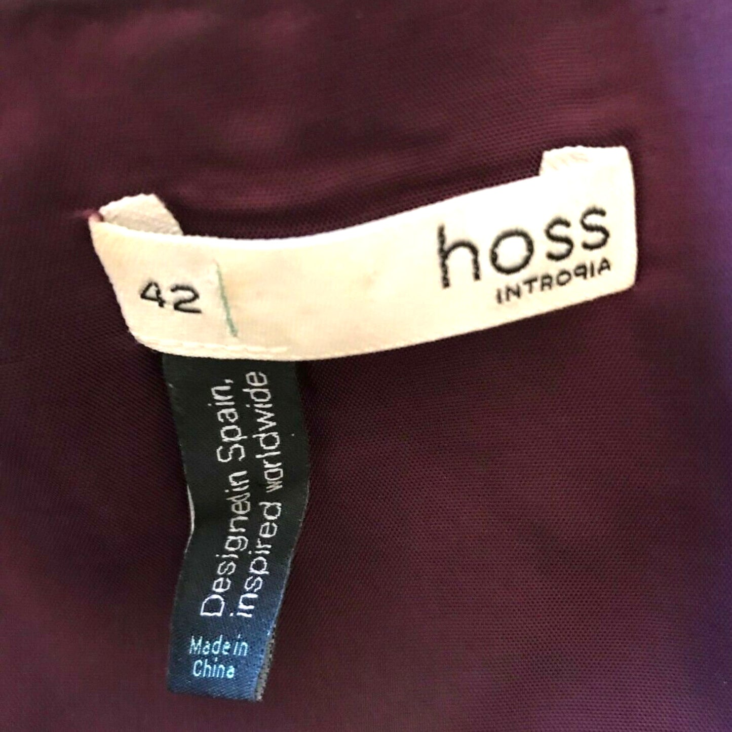 Close-up of a clothing tag with 'hoss' brand on a maroon fabric background