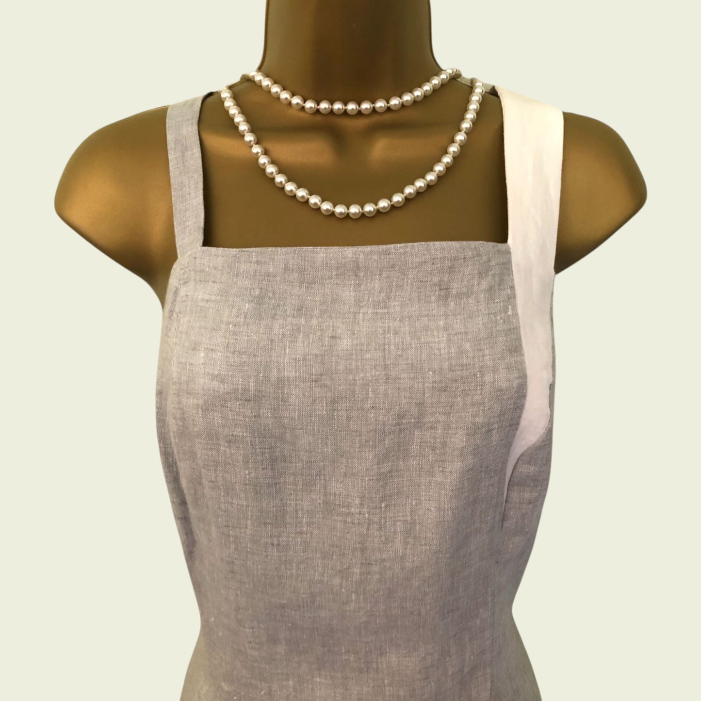 Mannequin wearing a gray apron with a pearl necklace on a light beige background