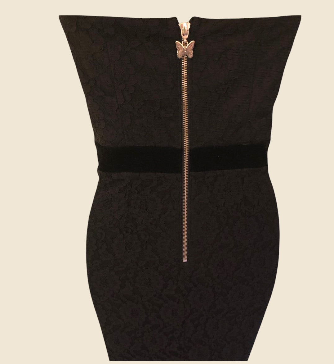 Black dress with a gold zipper and butterfly clasp on a beige background