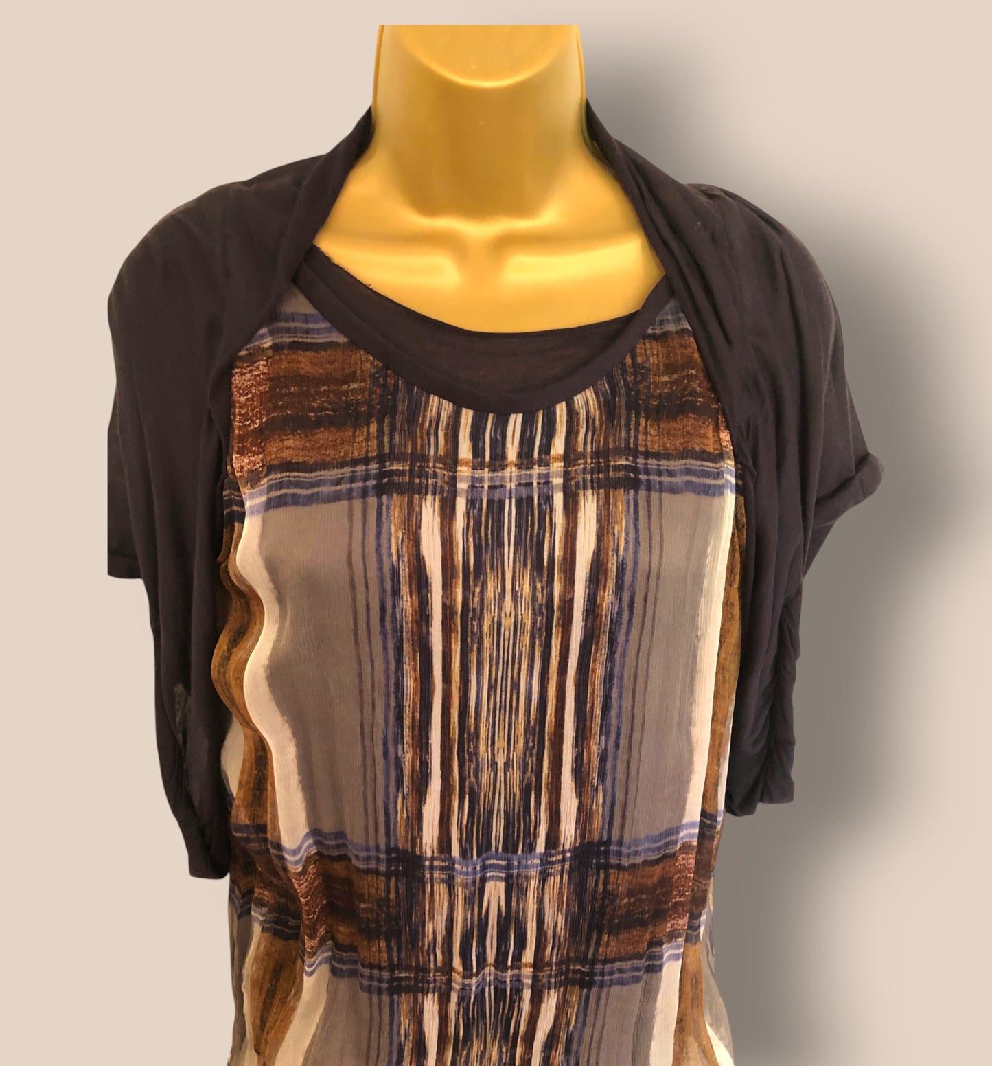 Mannequin wearing a brown and beige patterned dress with a black cardigan on a plain background