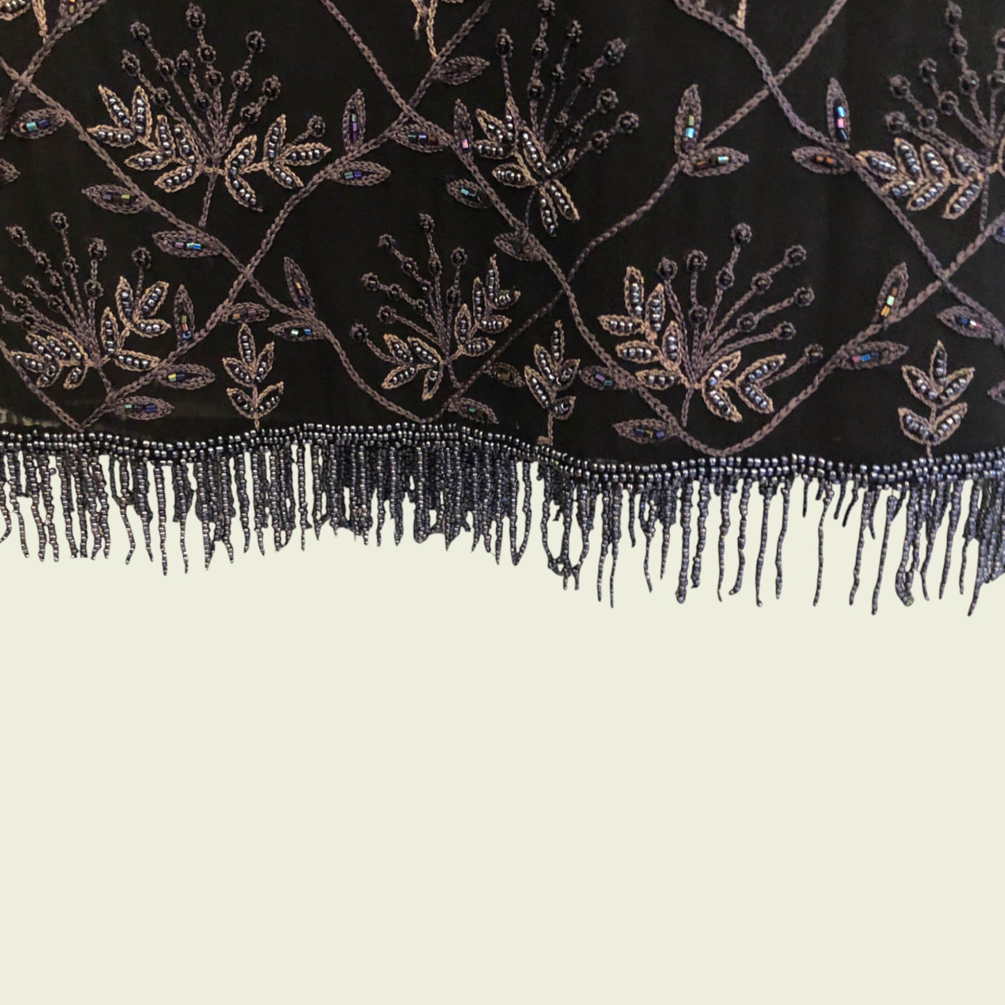 Close-up of a black fabric with intricate beadwork and fringes on a beige background