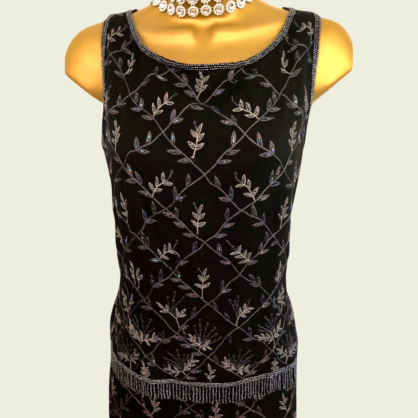 Black sleeveless top with silver leaf pattern on a mannequin against a beige background