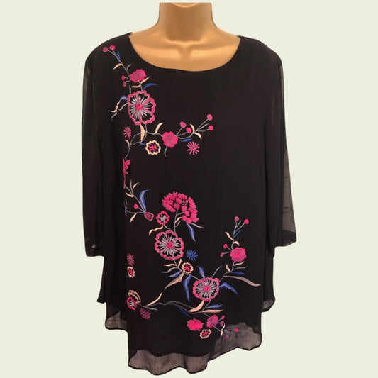 Black top with floral embroidery on a mannequin against a white background