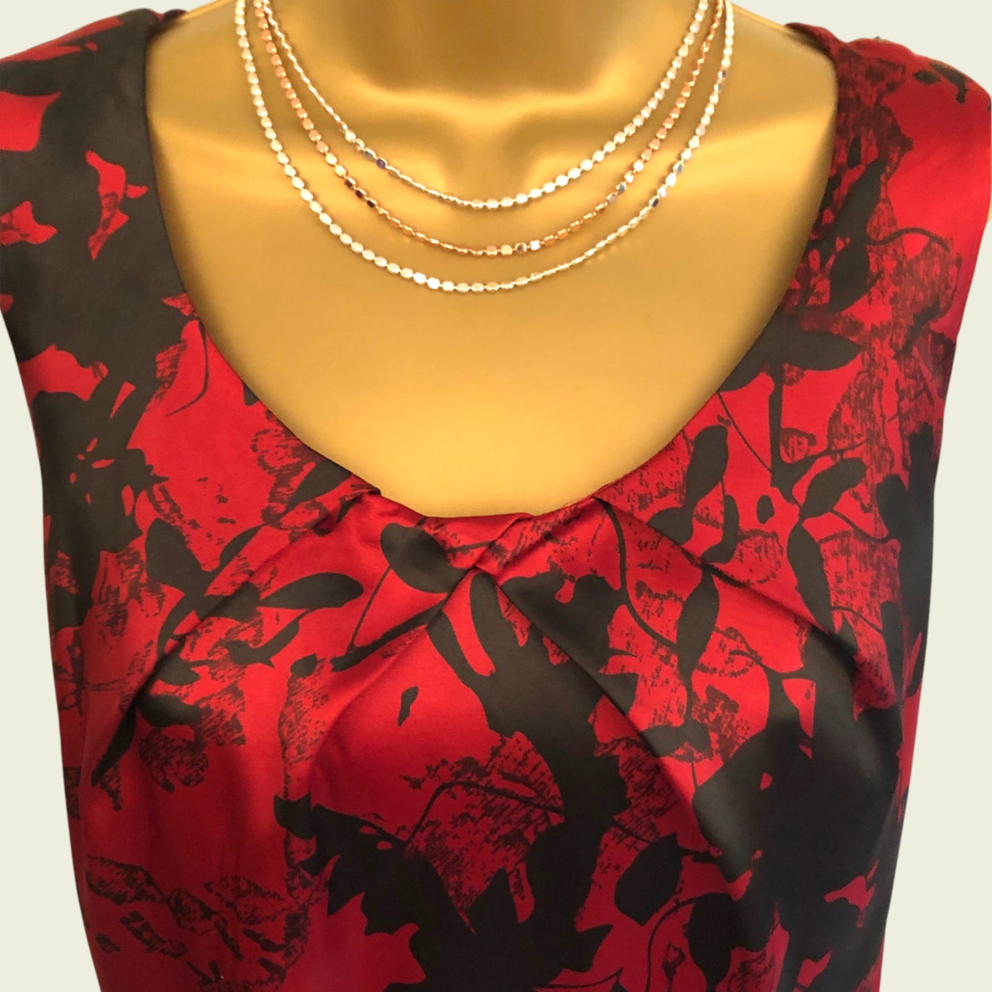 Mannequin wearing a red and black floral dress with gold necklaces.