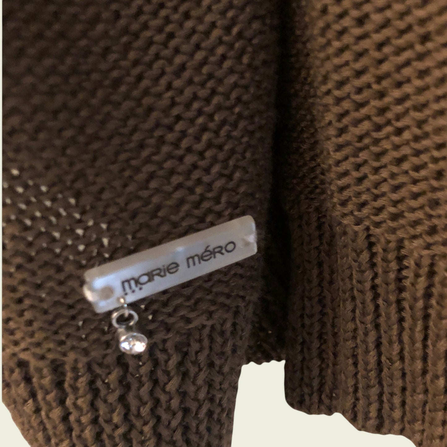Brown knitted sweater with 'Marie Méro' label on a beige background