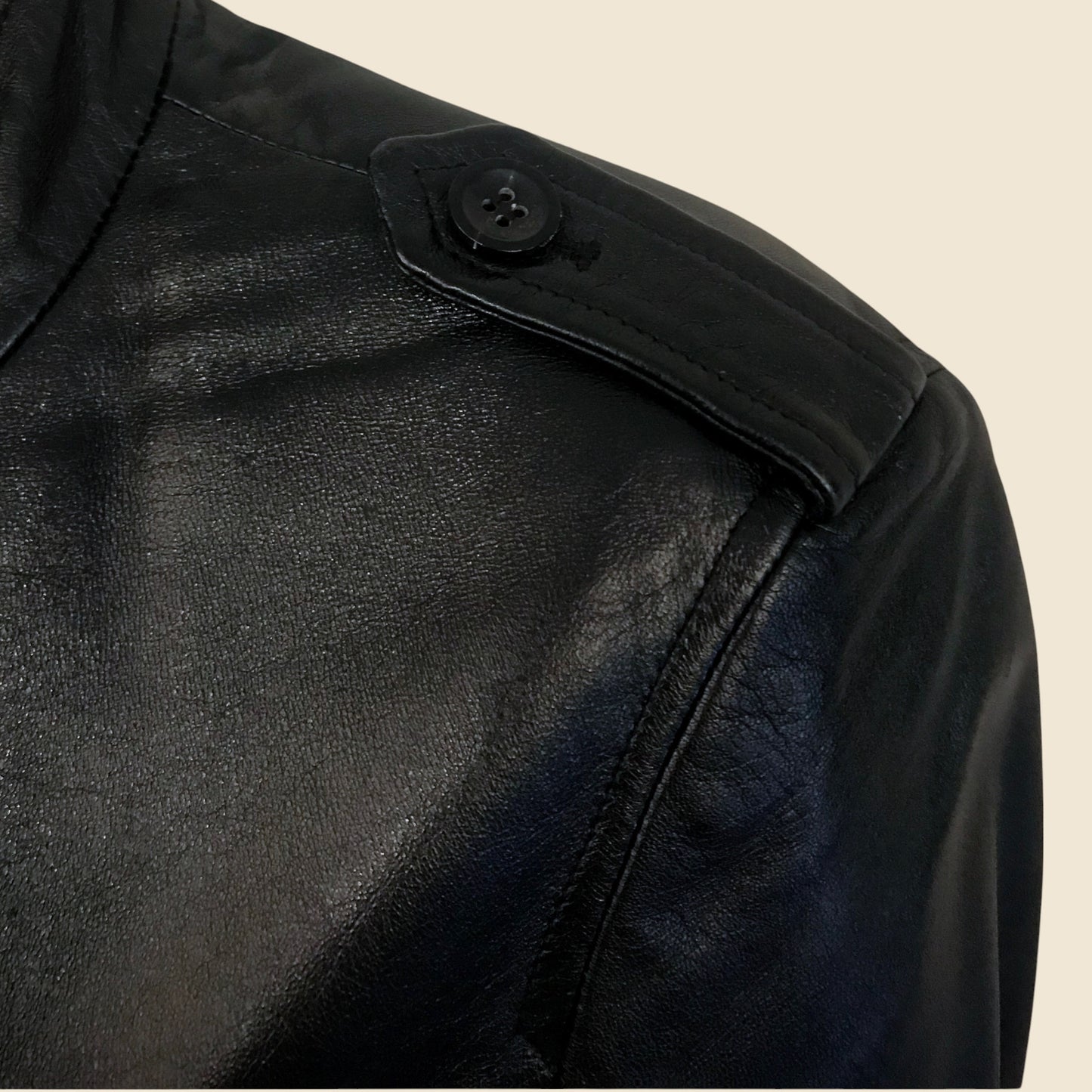 Close-up of a black leather jacket with a button on a beige background