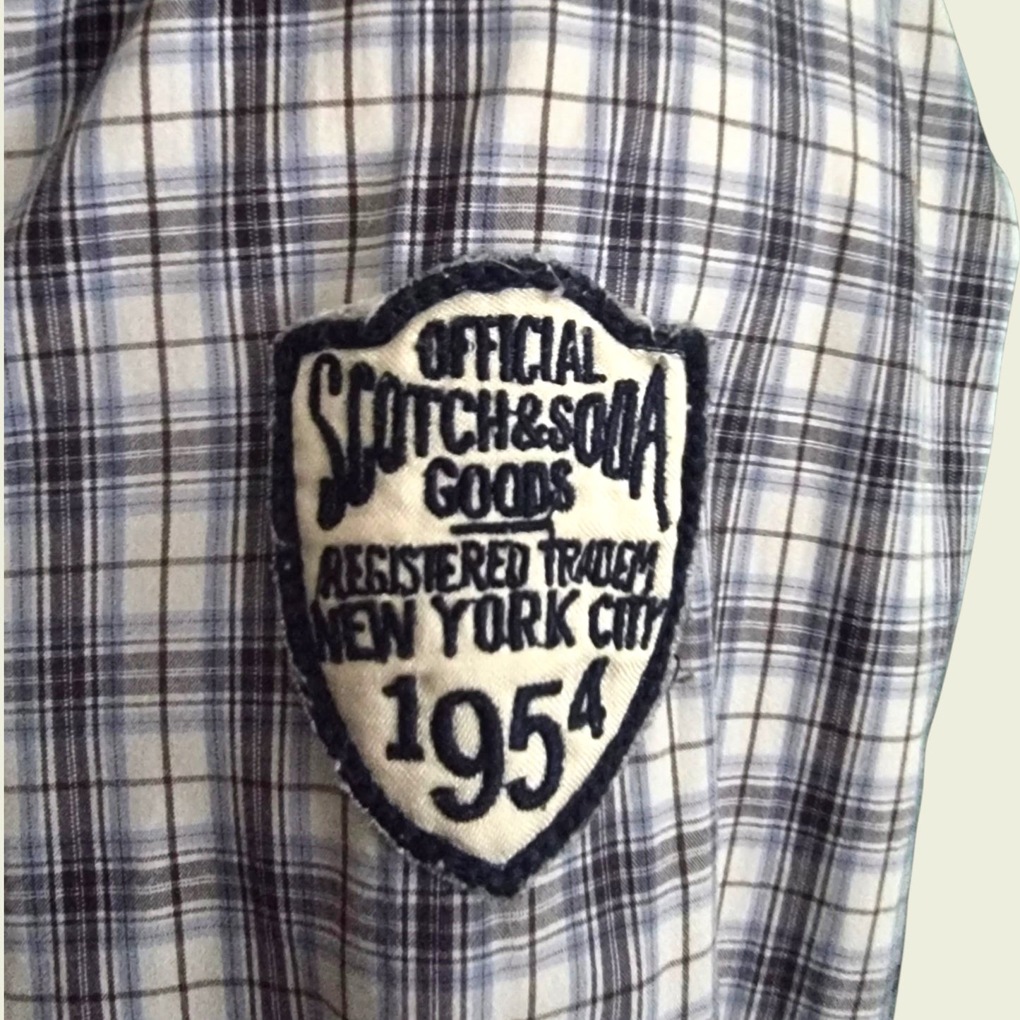 Plaid shirt with a patch reading 'Official Scotch & Soda Goods, Registered Trade New York City 1954'.