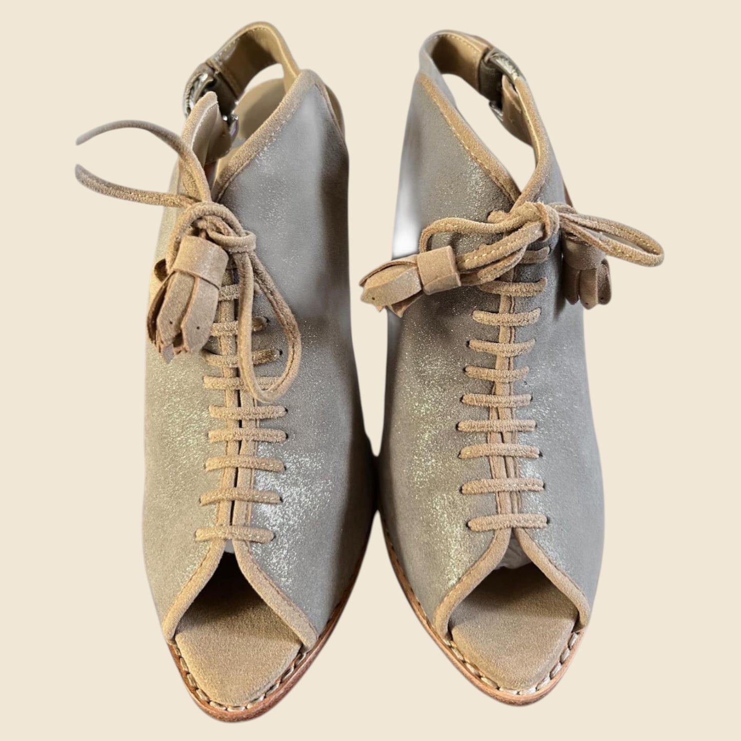 Pair of metallic beige open-toe shoes with beige laces on a beige background