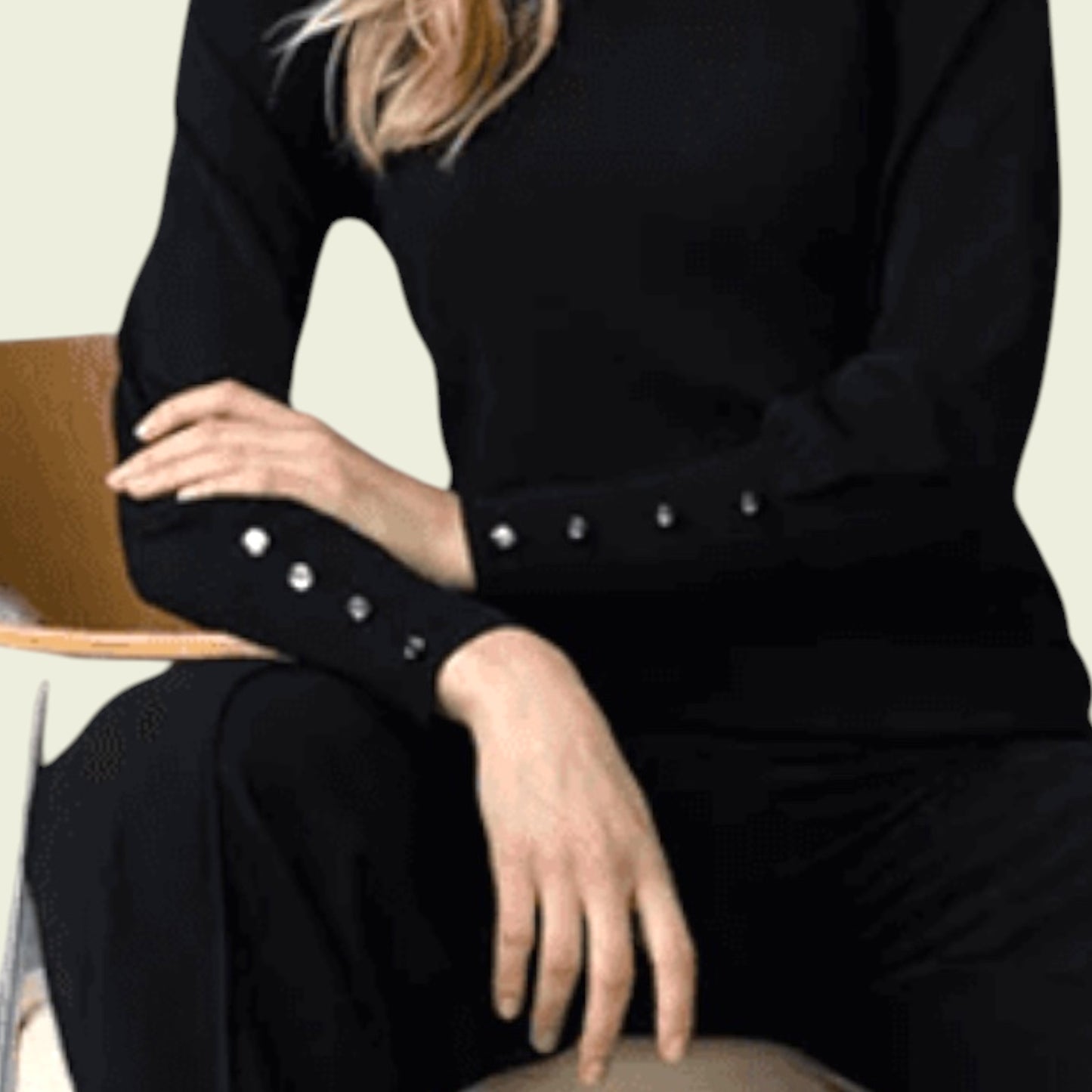Person wearing a black outfit with silver buttons sitting on a chair.