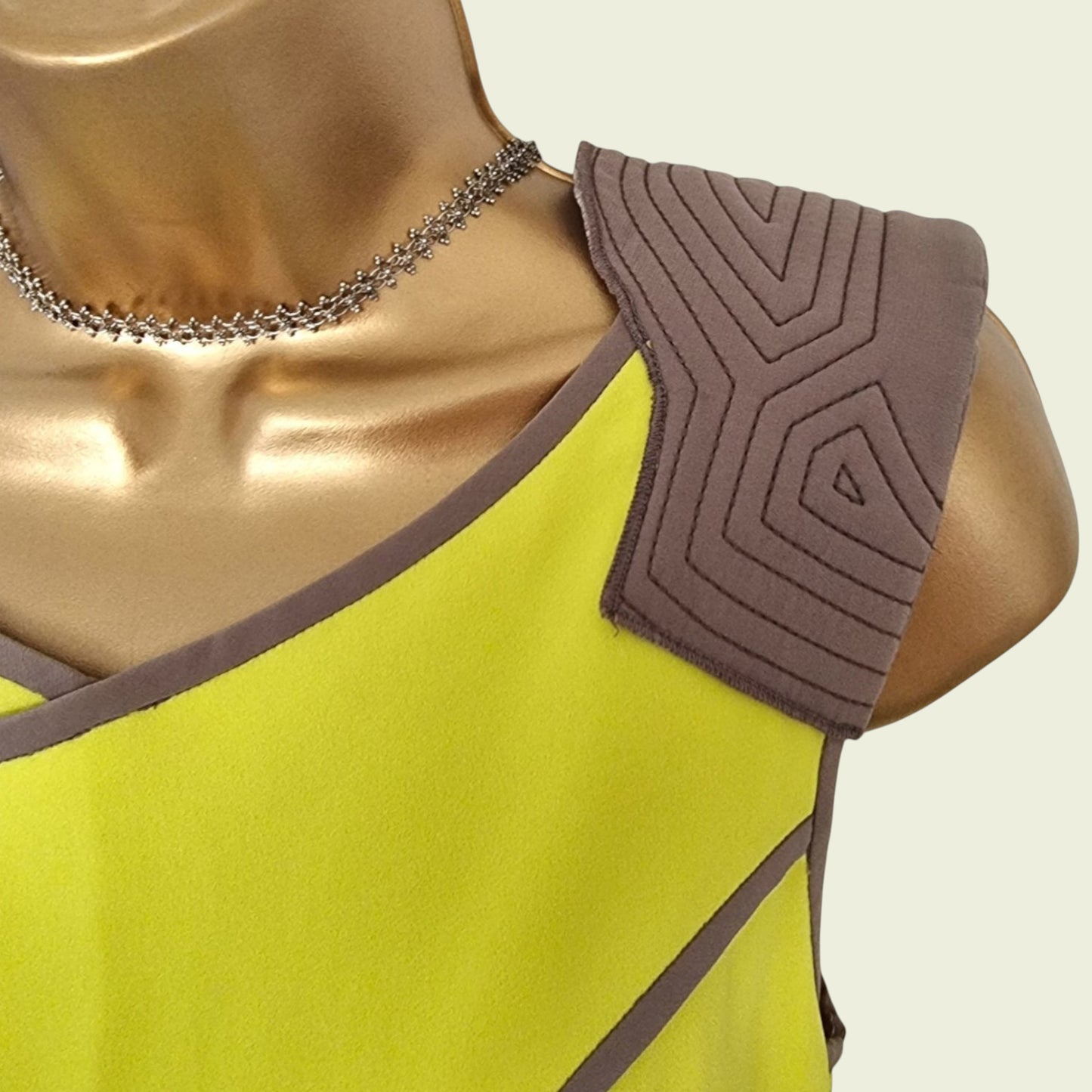 Mannequin wearing a yellow dress with brown geometric patterns on a beige background