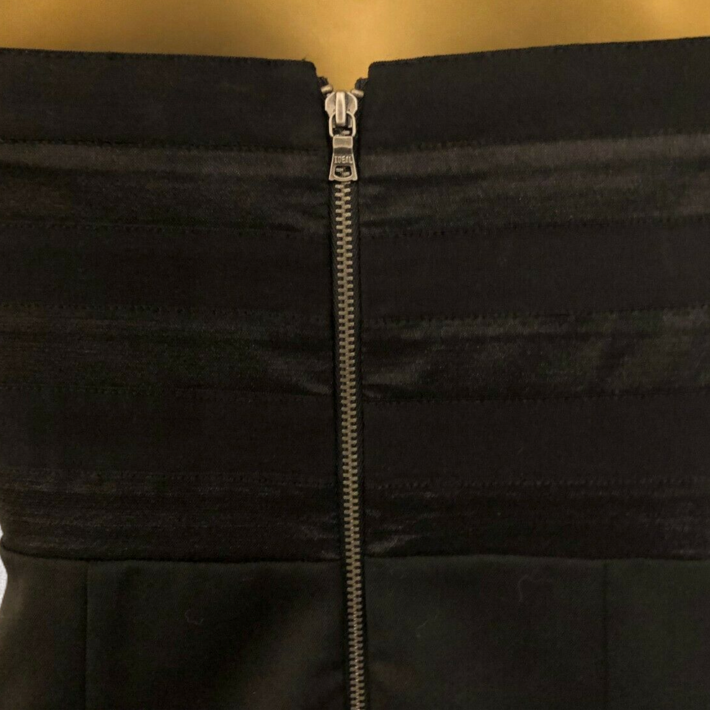 Close-up of a black dress with a zipper on a gold background