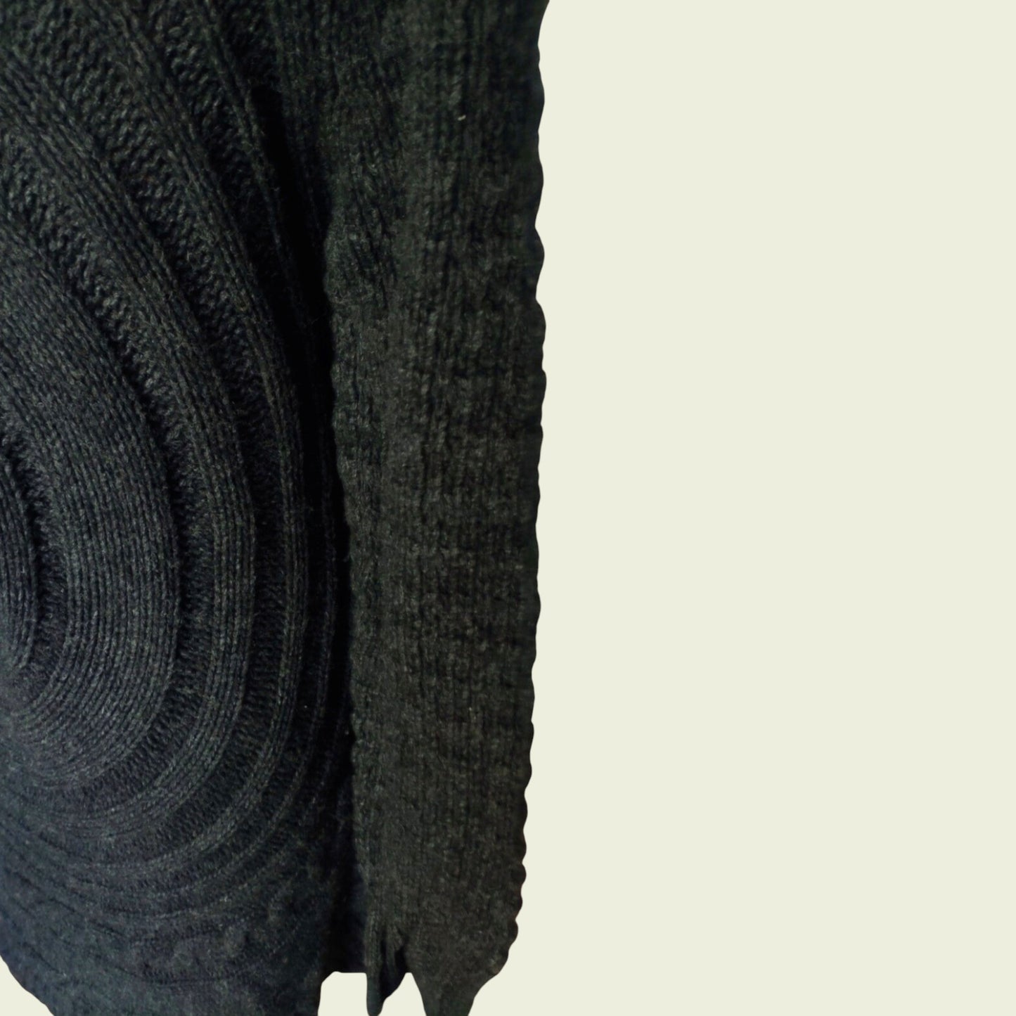 Close-up of a dark gray knitted sweater sleeve on a beige background