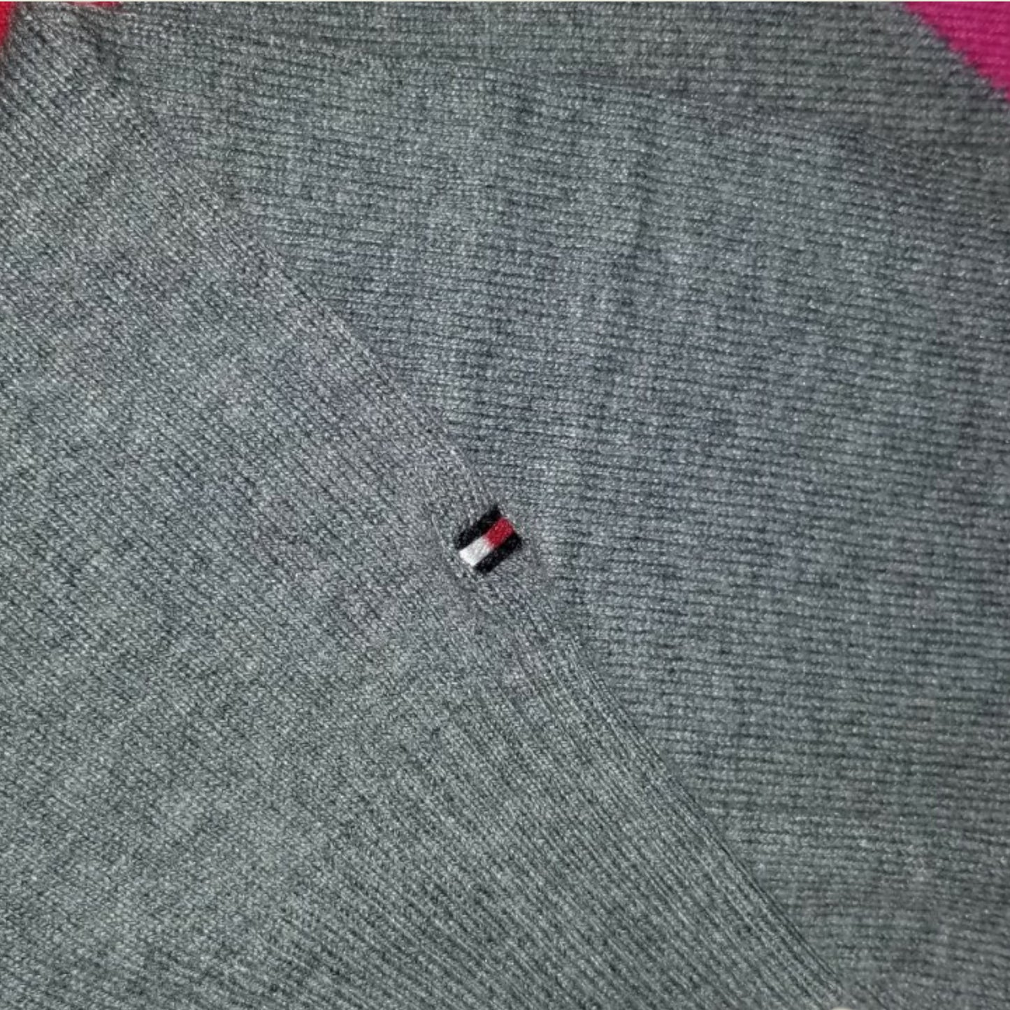 Close-up of a gray sweater with a small logo on the chest.