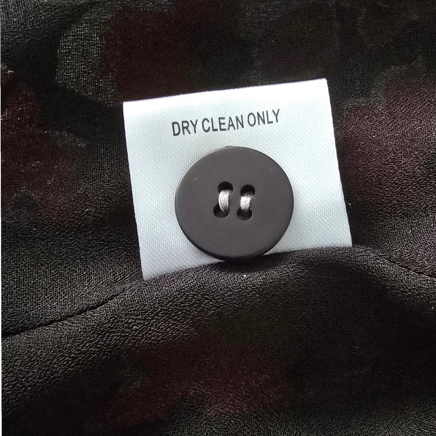 Black button on a label with 'Dry Clean Only' text on a dark fabric background