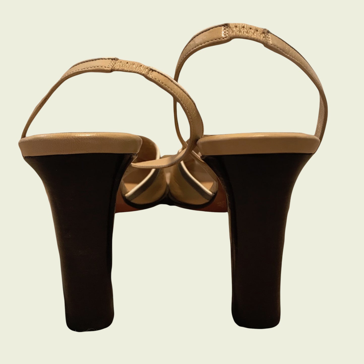 Pair of high-heeled shoes with tan straps on a beige background