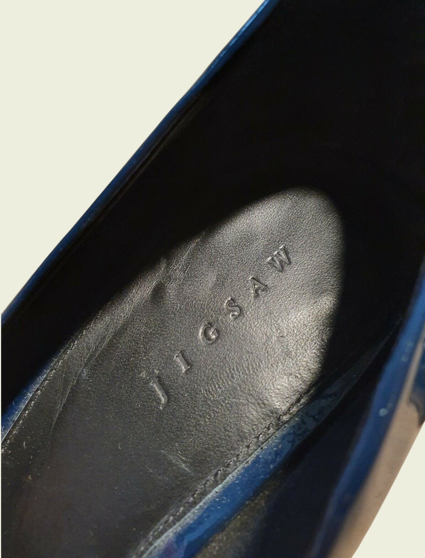 Close-up of a blue shoe with 'Jigsaw' branding on a beige background